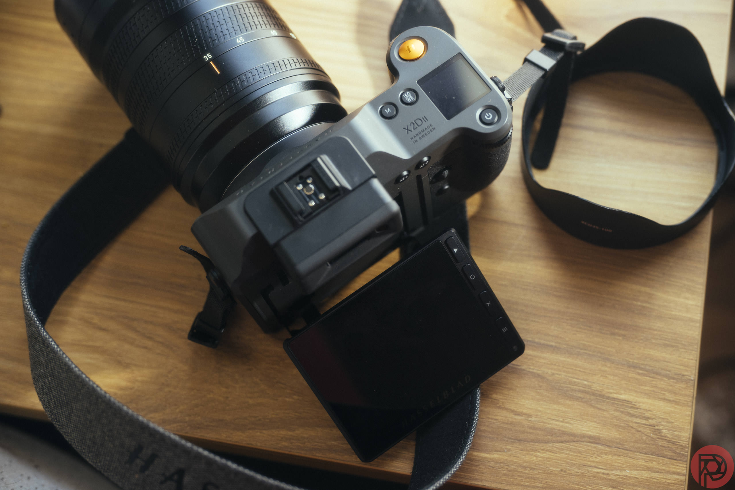 The Hasselblad X2D II 100C Got a Major Upgrade, Sort Of A Hasselblad X2D camera with a strap and flip-out screen rests on a wooden surface.