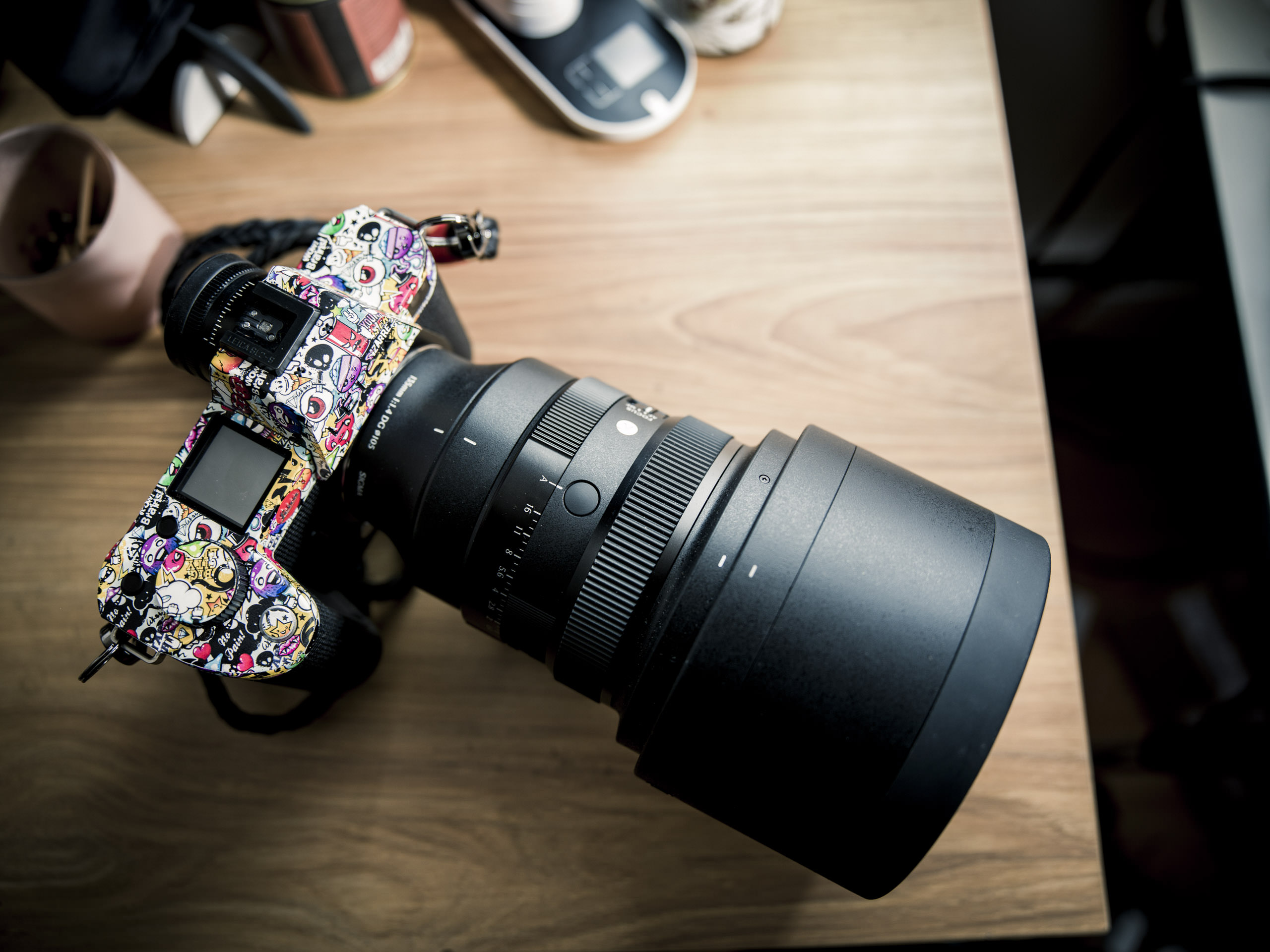 A camera with a colorful, sticker-covered body and a large lens rests on a wooden desk.