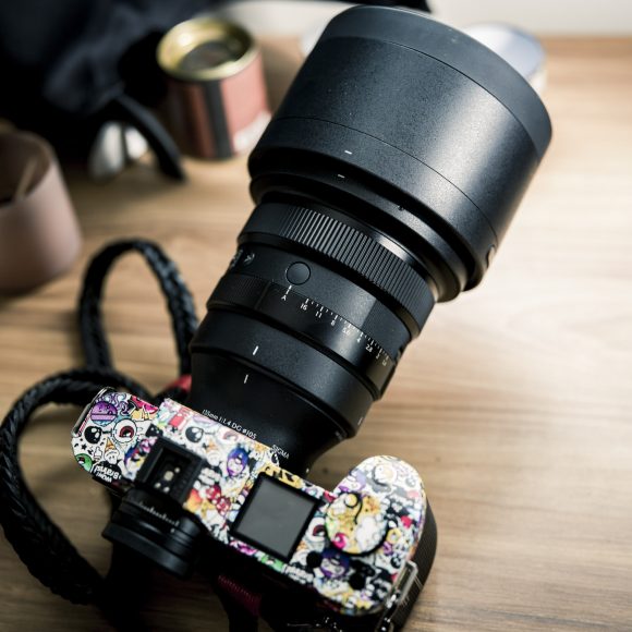 A camera with a large lens and a body covered in colorful stickers sits on a wooden surface.