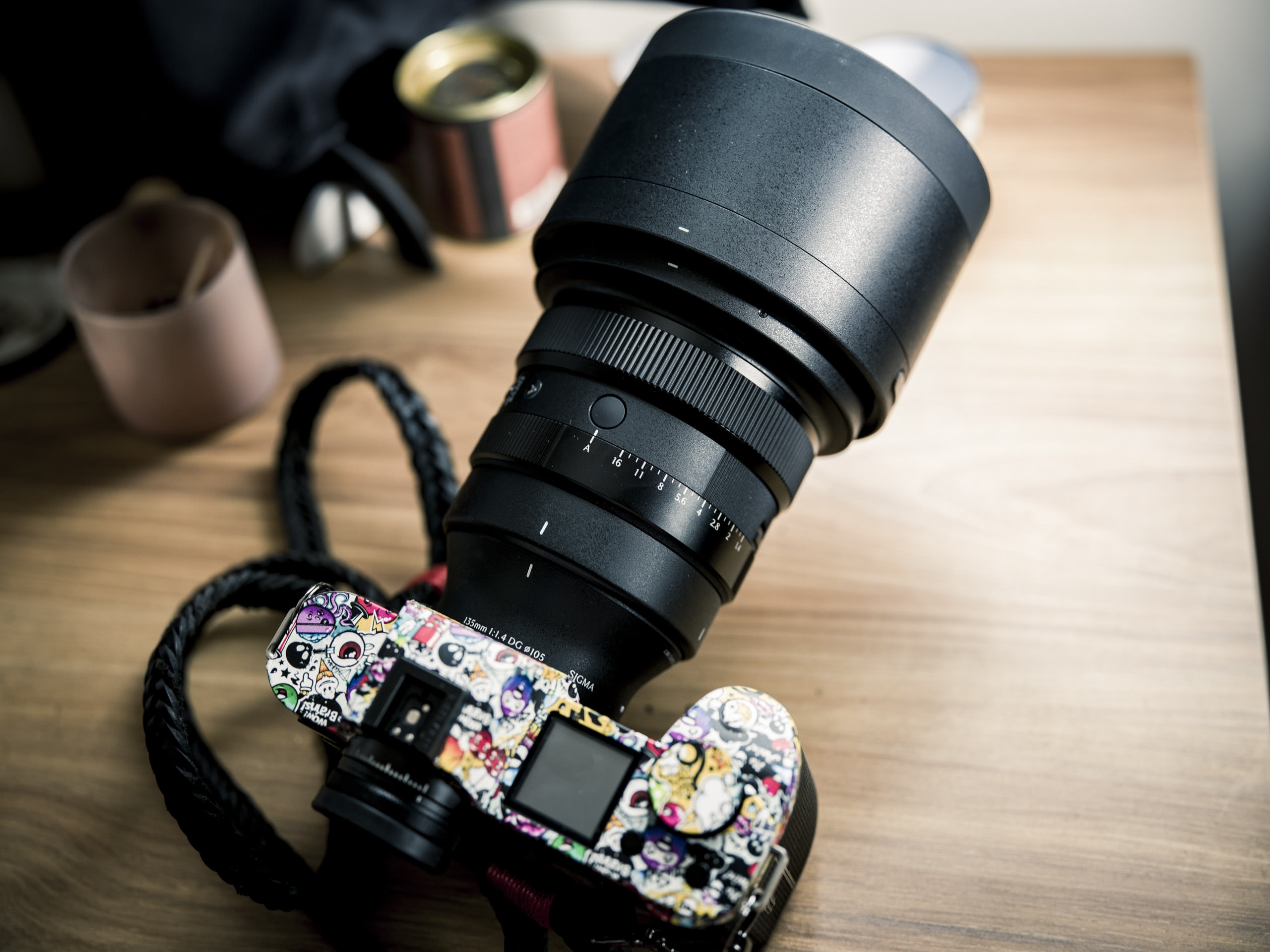 The Things About Sigma Lenses You Probably Never Knew A camera with a large lens and a body covered in colorful stickers sits on a wooden surface.