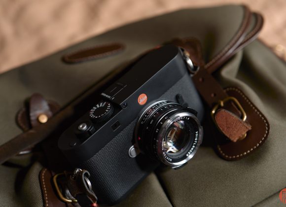 A black Leica camera rests on an olive green canvas bag with brown leather straps.