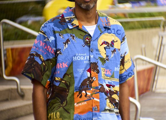 Man in colorful Polo shirt, white bucket hat, and sunglasses standing outdoors near steps.
