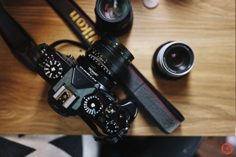 Top view of a Nikon camera with lens, two additional lenses, and a camera strap on a wooden surface.