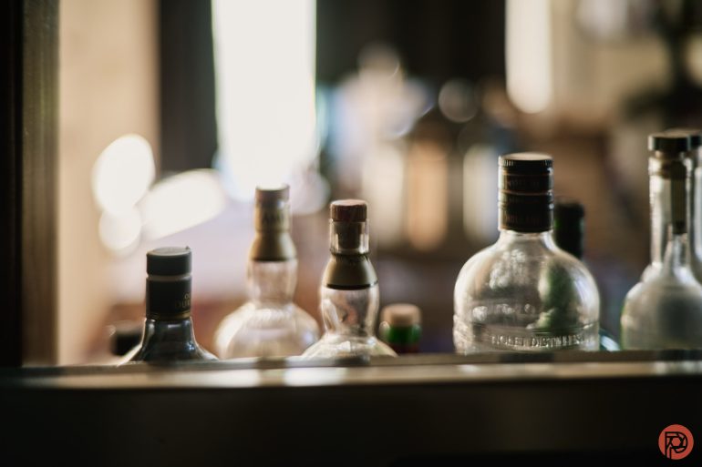 Several glass bottles with caps are lined up on a surface, photographed in soft, natural light.