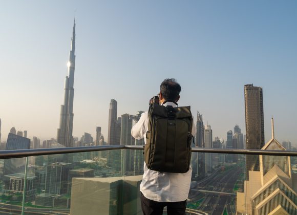 Person with backpack taking a photo of a city skyline with tall modern buildings and clear sky.