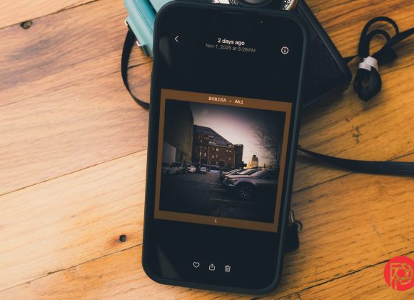 A smartphone on a wooden surface displays a photo of parked cars beside a brick building.
