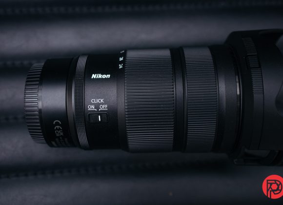A Nikon camera lens with focus and zoom rings, shown on a dark background.