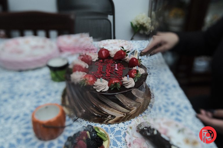 A hand cuts a chocolate cake with strawberries and birthday icing on a decorated table.