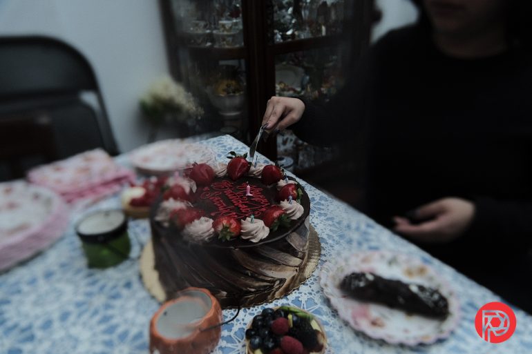 A person cuts a chocolate cake topped with strawberries and icing on a decorated table.