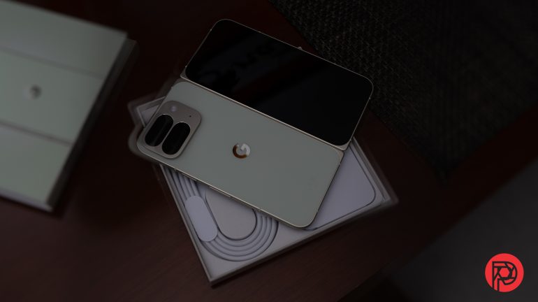 A foldable smartphone with dual cameras rests on its partially opened box, showing a charging cable inside.