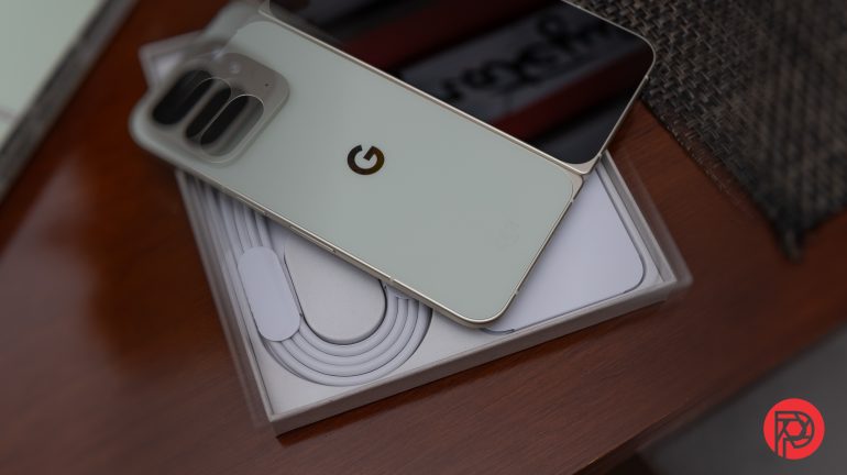 A Google Pixel phone rests on its box with a charging cable, on a wooden surface.