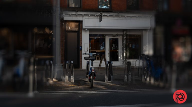 A single bike is parked at a bike-sharing station on a city sidewalk in front of a closed storefront.