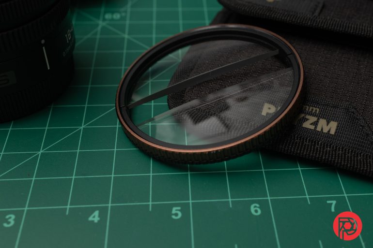 A split diopter lens filter on a green cutting mat next to a black lens pouch and camera lens.