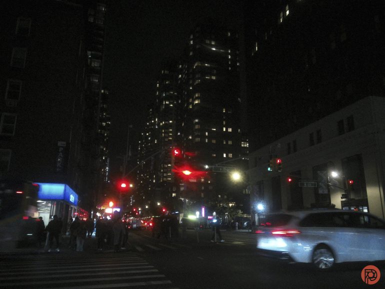 Nighttime city street scene with cars, traffic lights, and tall buildings with illuminated windows.