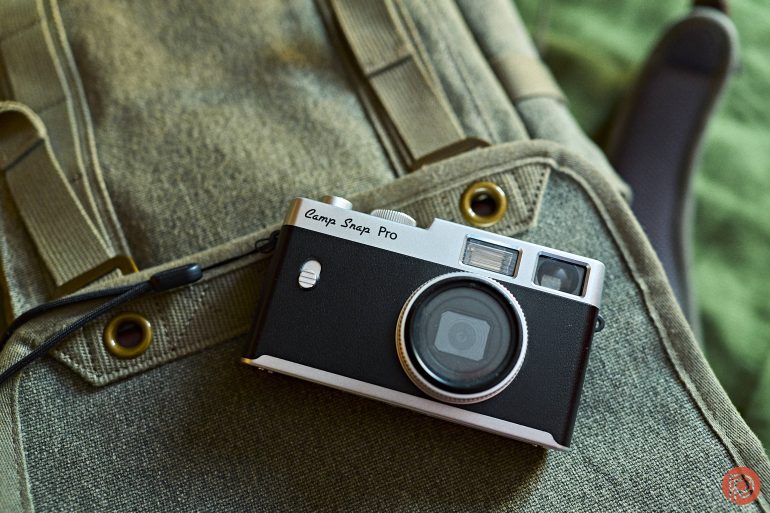 A compact black and silver camera labeled Camp Snap Pro rests on a green canvas bag.