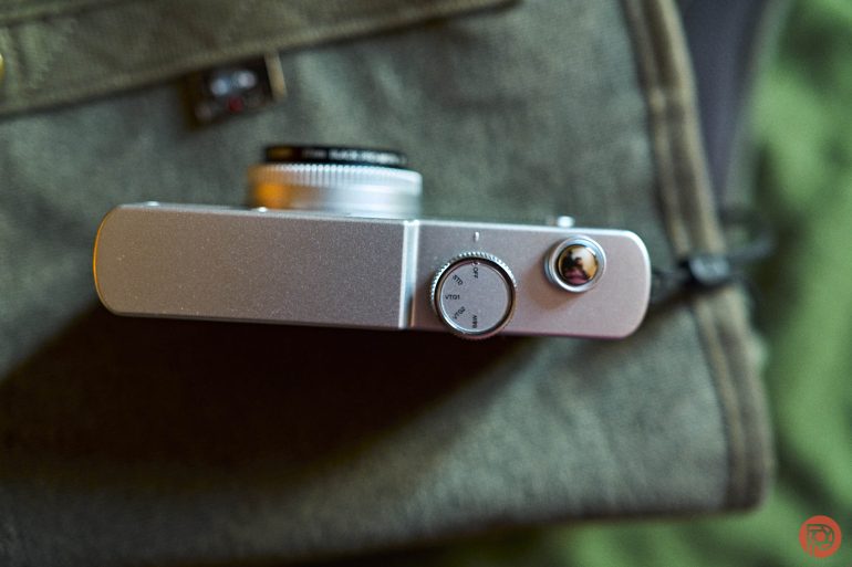 Top view of a silver camera with a dial, placed on a green fabric surface.