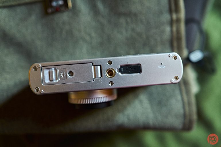 Close-up of the bottom of a silver digital camera showing battery, tripod mount, and reset button.