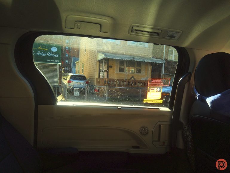 View from inside a car looking out a window at a house, car, and signage across the street.
