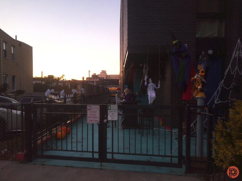A gated yard decorated with ghosts, witches, and cobwebs for Halloween at sunset.