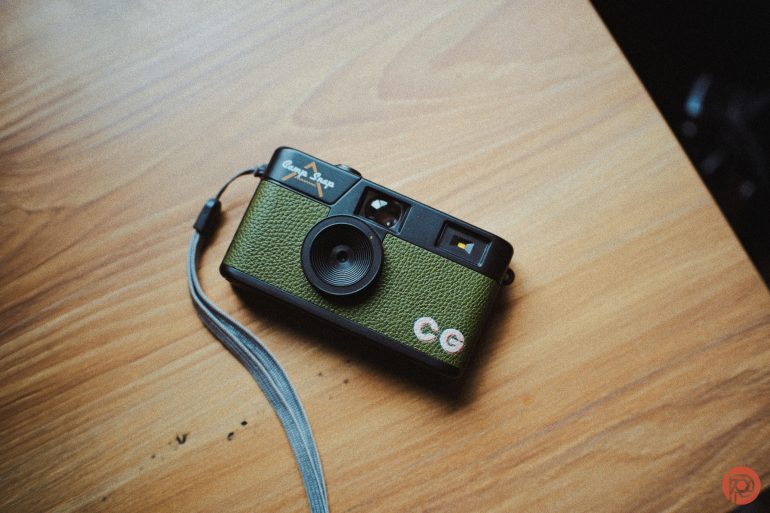 A green vintage film camera with a wrist strap rests on a wooden surface.
