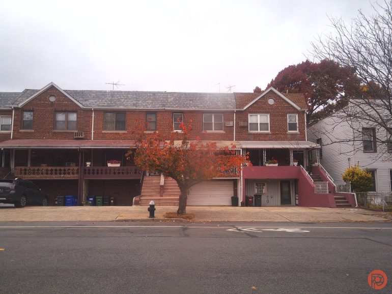 A small tree with orange leaves stands in front of brick row houses on a cloudy day.