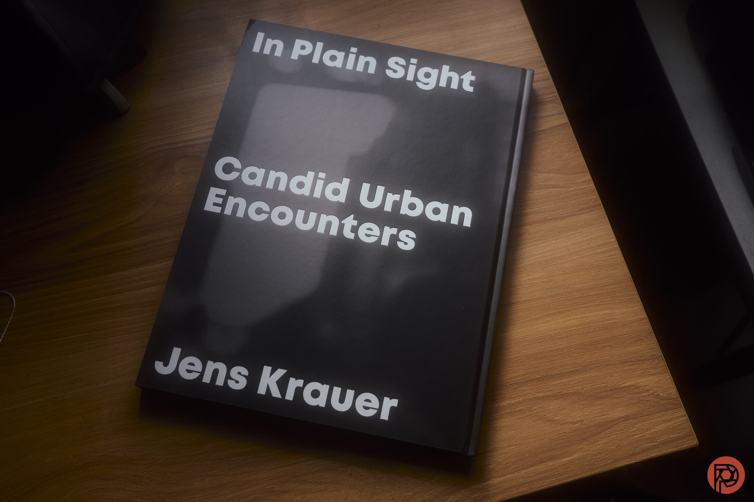 A book titled In Plain Sight: Candid Urban Encounters by Jens Krauer on a wooden surface.