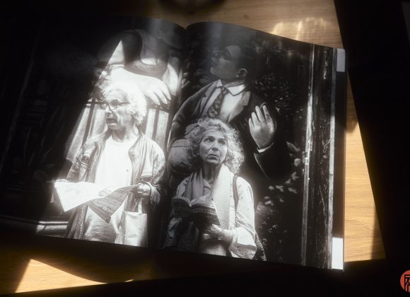 Black and white photo book open to a page showing two elderly people holding papers, with dramatic lighting.