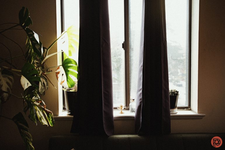 Large window with dark curtains, potted plants on the sill, and sunlight streaming into a cozy room.