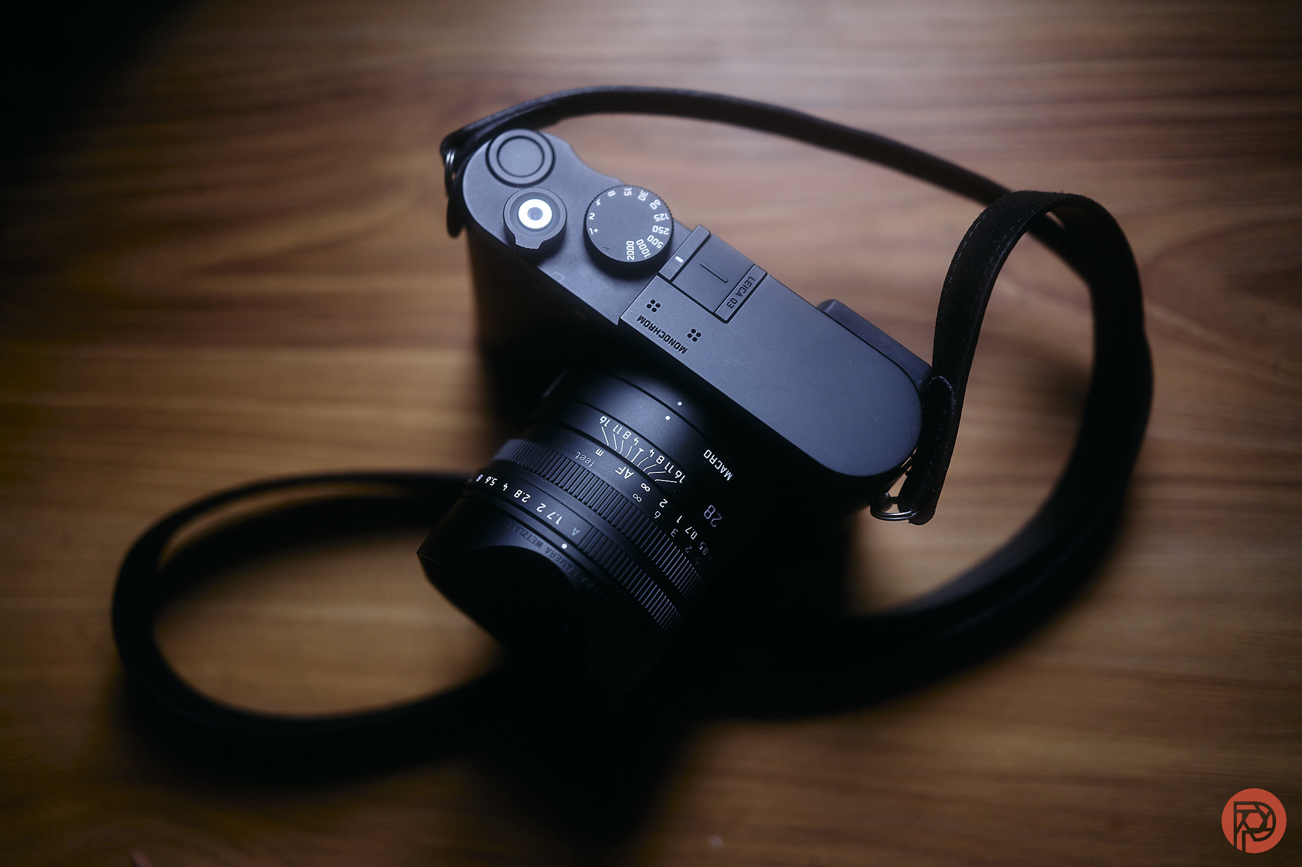 A black camera with a lens and strap rests on a wooden surface under soft lighting.