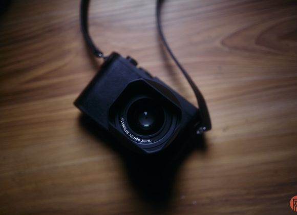 A black camera with a strap placed on a wooden surface, seen from above.
