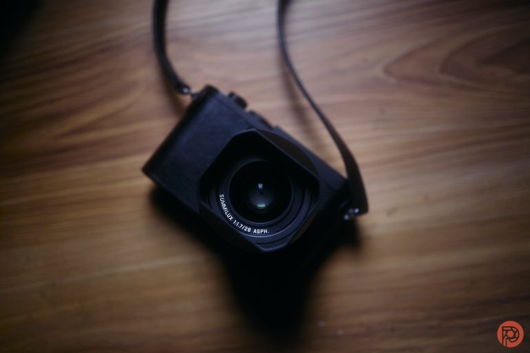 A black camera with a strap placed on a wooden surface, seen from above.