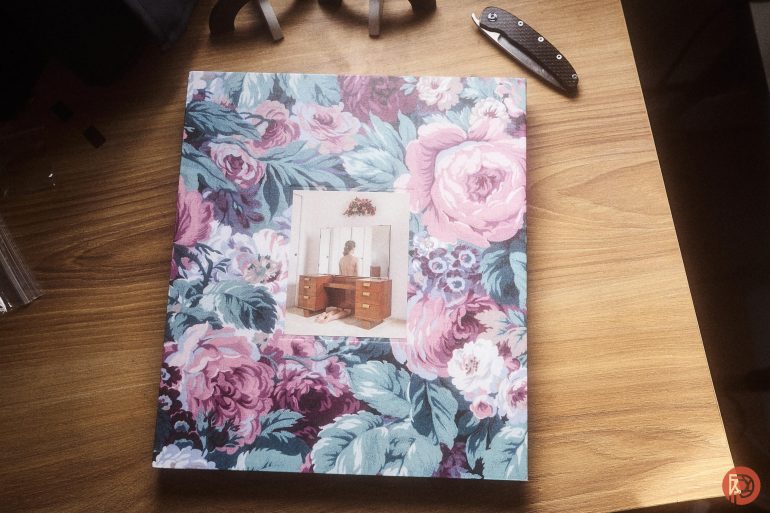 A floral-patterned book with a vintage photo on a wooden desk next to a folding knife.