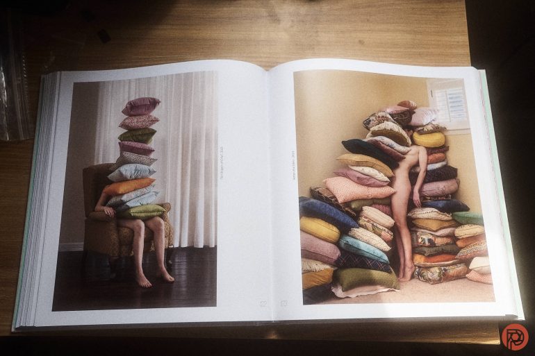 Open book showing photos of people mostly hidden under stacks of colorful pillows on chairs.