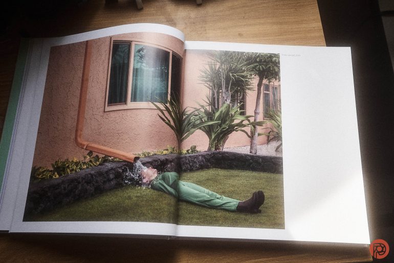 A book shows a photo of a person lying on grass, appearing to have water pouring on their head from a window ledge.