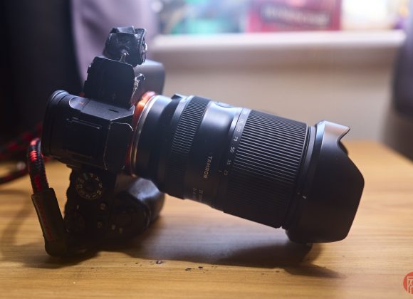 A black Sony camera with a zoom lens sits on a wooden surface in soft natural light.