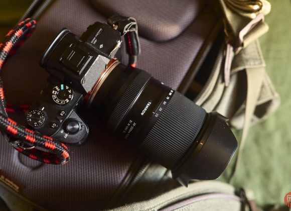 A Sony camera with a Tokina lens rests on a gray camera bag with a red and black strap attached.
