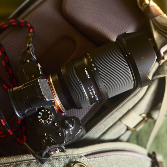 A black Sony camera with a Tamron lens rests on a padded green camera bag, strap attached.