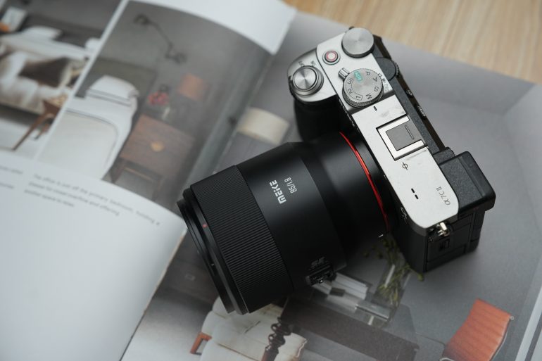 A digital camera with a Meike lens rests on an open magazine featuring interior designs.