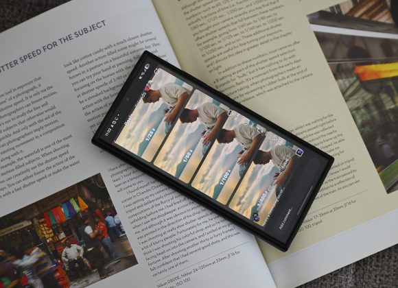 A smartphone on magazine pages displays a social media post of a man by a railing at sunset.
