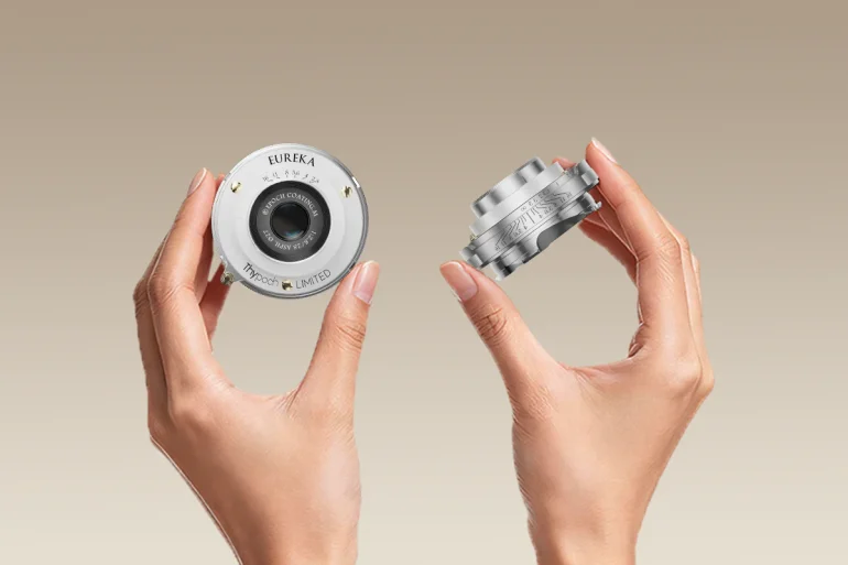 Two hands holding small, silver camera lenses against a plain beige background.