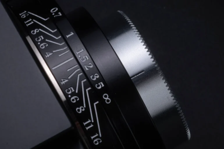Close-up of a black camera lens with focus and aperture markings in white on a dark background.