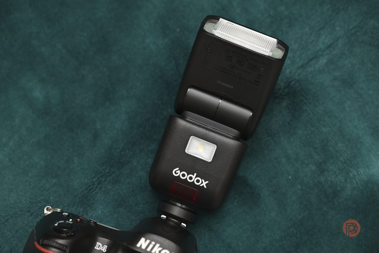 A Godox camera flash attached to a Nikon camera on a teal textured surface.