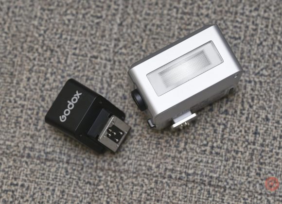 A Godox camera flash trigger and a small silver camera flash unit on a textured gray surface.