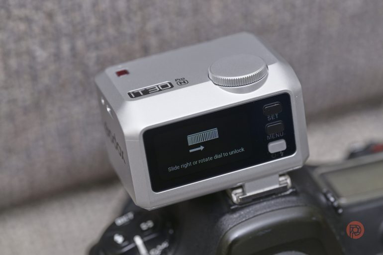 A close-up of a digital camera with a small screen instructing to unlock by sliding right or rotating dial.