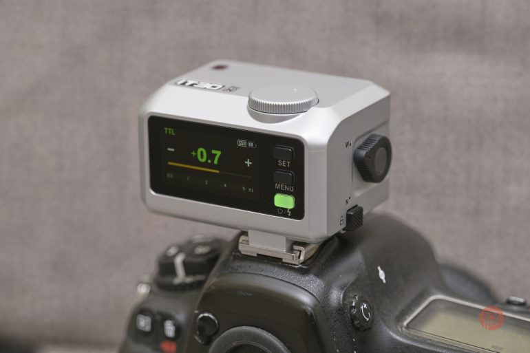 A close-up of a camera with a digital flash trigger mounted on top, displaying a -0.7 setting.