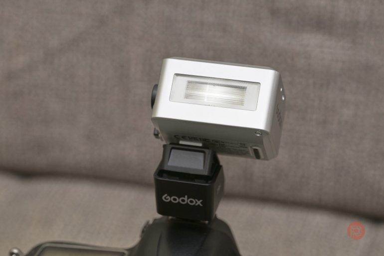 A Godox camera flash mounted on a camera against a blurred, neutral background.