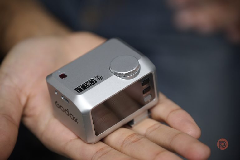 A hand holding a compact silver Godox camera accessory labeled TT20 RC with a control dial.