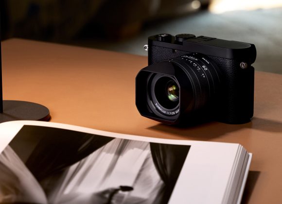 A black camera sits on a brown table beside an open book displaying a black and white photo.