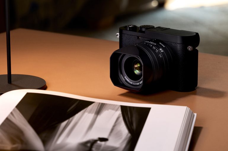 A black camera sits on a brown table beside an open book displaying a black and white photo.