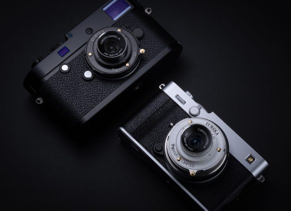 Two vintage-style cameras, one black and one silver, placed side by side on a dark background.
